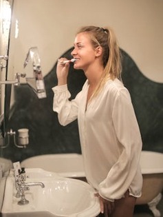woman brushing her teeth and looking in mirror